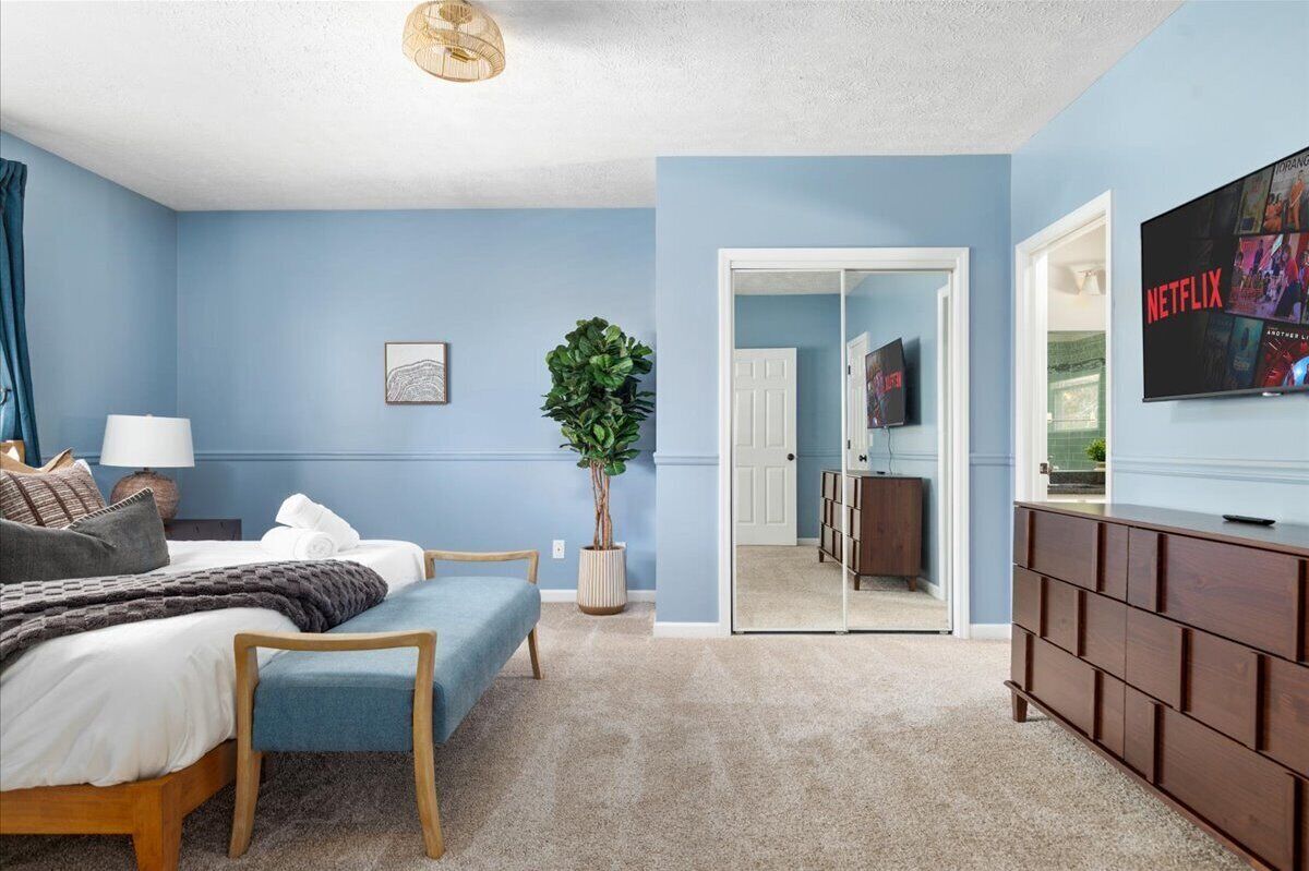A bedroom with a bed, bedside table, lamp, and a large potted plant.