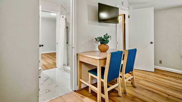 A room with a wooden floor, a wooden table with two blue chairs, a potted plant, and a flat-screen TV mounted on the wall. - Luxury Carmel Suite  Walk 25 min walk  Carmel Beach 109 (Carmel)