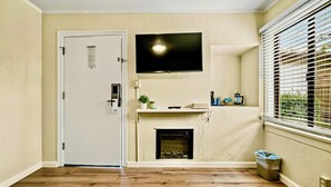A room with a white door, a fireplace, a mounted TV, and a window with blinds. - Luxury Carmel Suite  Walk 25 min walk  Carmel Beach 109 (Carmel)