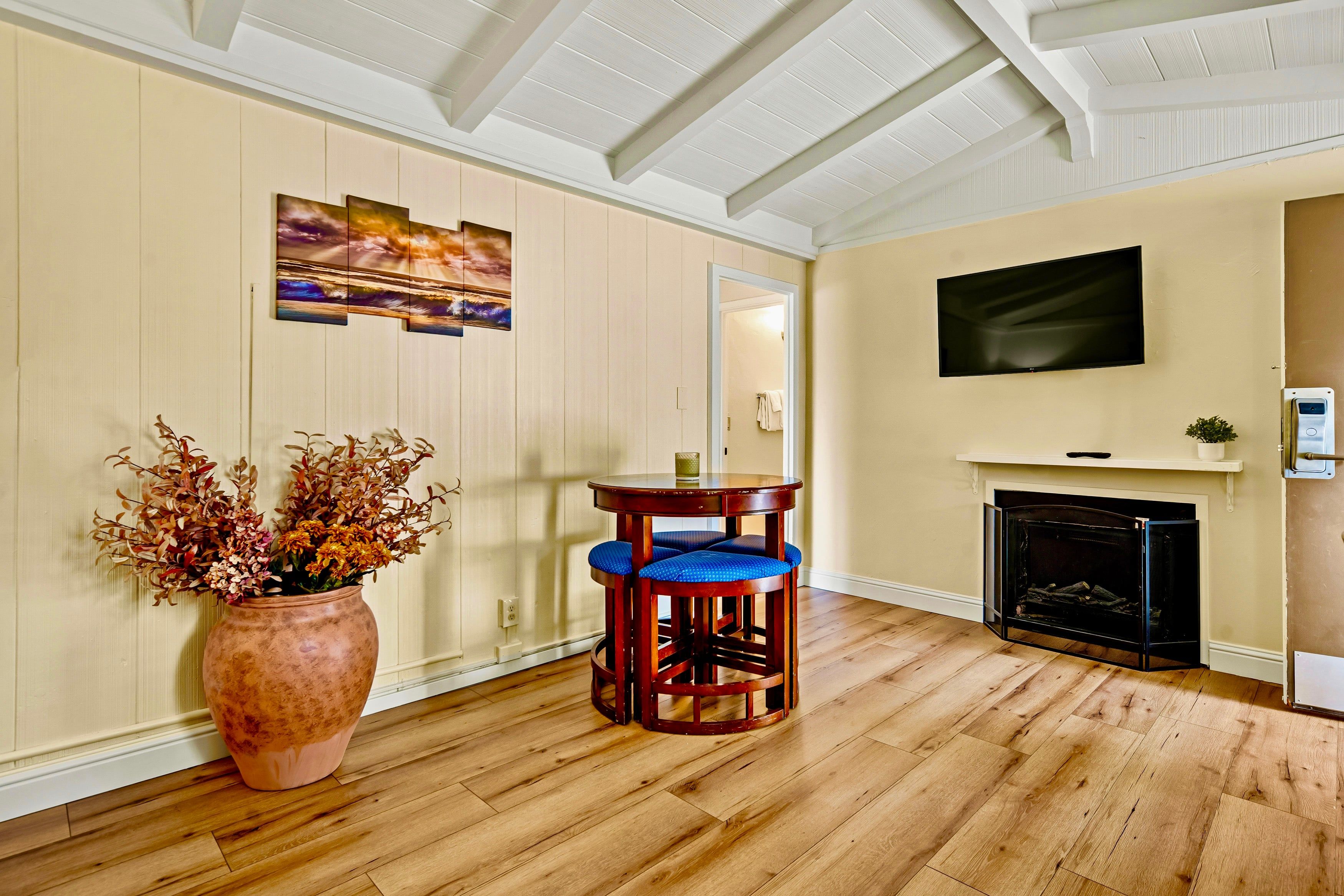 Un salon doté d’un plancher en bois, d’une cheminée, d’un téléviseur fixé au mur et d’une table entourée de chaises à coussins bleus.