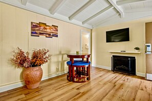 Un salon doté d’un plancher en bois, d’une cheminée, d’un téléviseur fixé au mur et d’une table entourée de chaises à coussins bleus.