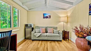 Ein gemütliches Wohnzimmer mit einer Couch, einem Fernseher, einer Lampe und einem großen Fenster mit Jalousien.