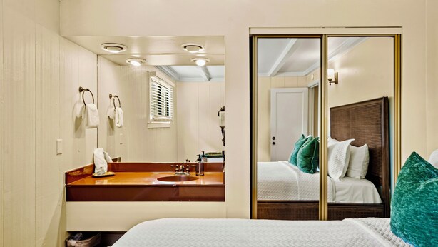 Ein Hotelzimmer mit einem großen Bett, einem Holz-Kopfteil, einem Badezimmer mit Waschbecken und Spiegel sowie einem Kleiderschrank mit Spiegel.