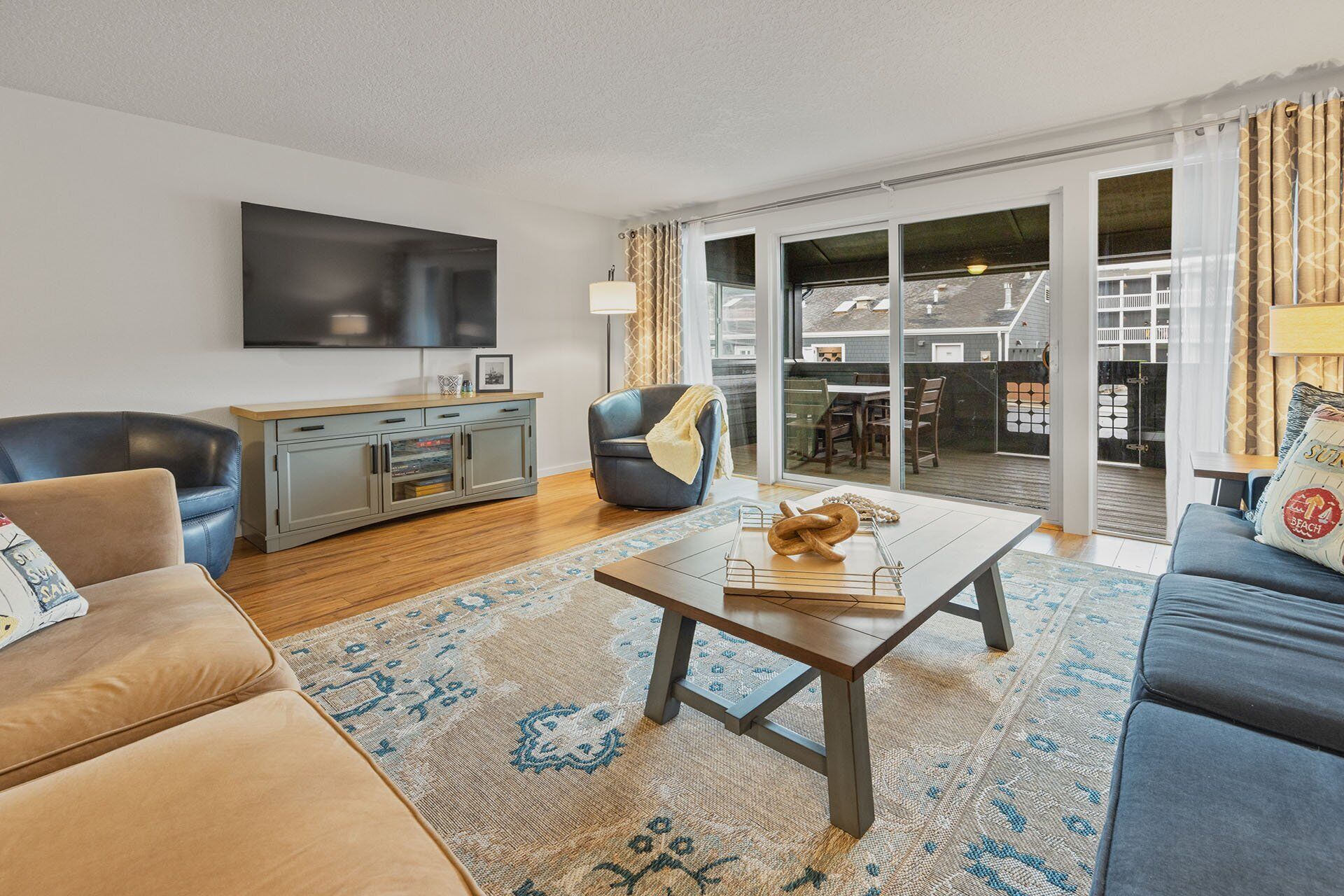 A modern living room with a sofa, a coffee table, and a TV. There is a sliding glass door leading to a balcony.