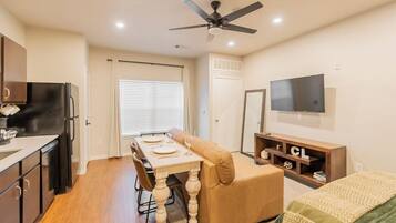 A compact living space with a kitchenette, dining area, and a TV mounted on the wall.
