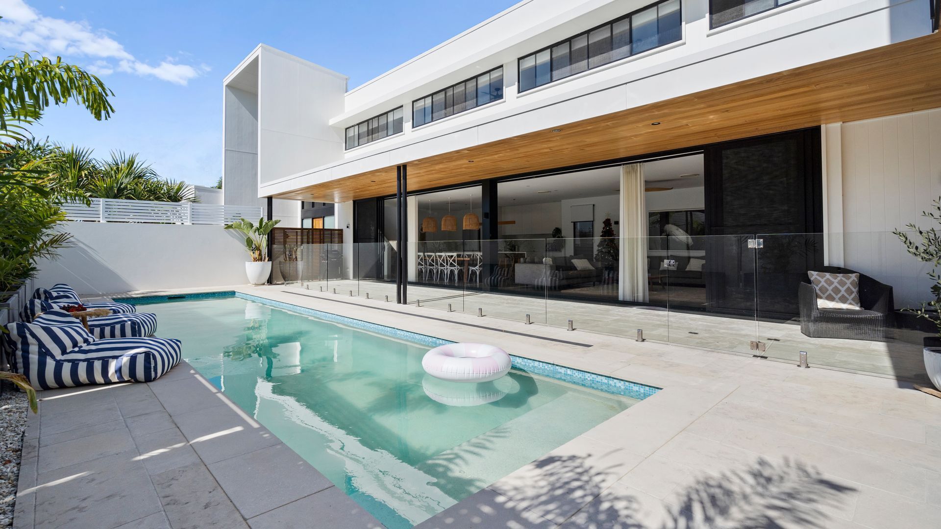 A modern house with a swimming pool, outdoor seating, and a large glass door leading to the interior.