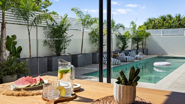 Escena junto a la piscina con una mesa dispuesta para una comida, una bebida y una planta de cactus.