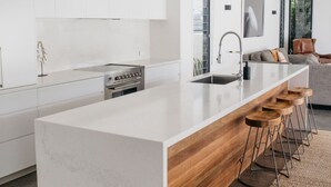 Una cocina moderna con una isla grande, electrodomésticos de acero inoxidable y un espacio con taburetes de madera.