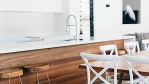 Una cocina moderna con armarios blancos y encimera de madera. Se observan sillas blancas alrededor de una mesa de comedor de madera.