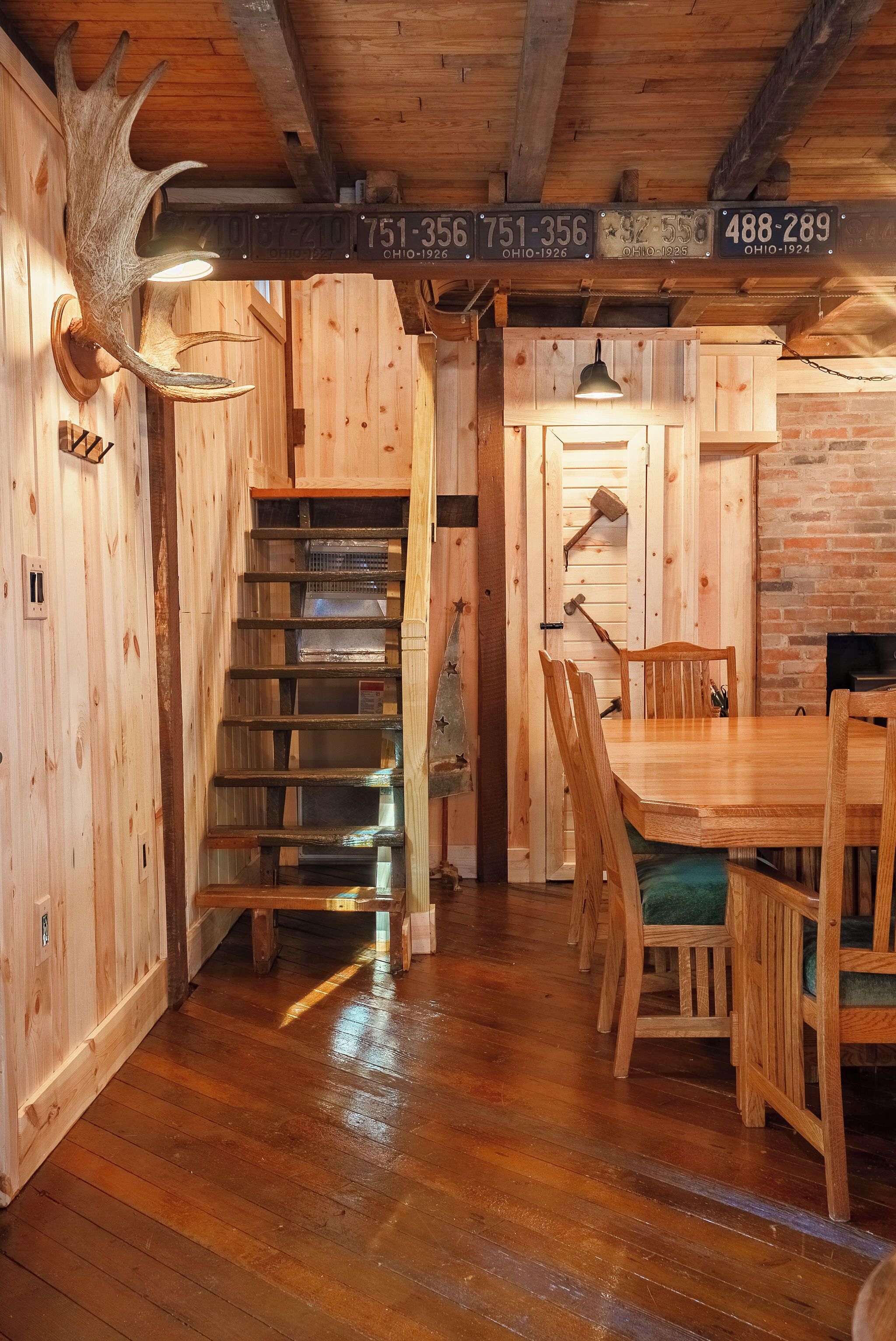 A wooden interior with a staircase, a dining table with chairs, and a mounted deer head.