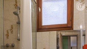 Un baño con cabina de ducha de vidrio, cortina de ducha blanca, un gabinete de madera sobre el lavamanos y un espejo.