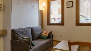 Una sala de estar moderna con un sofá gris, almohadones de colores, una mesa de centro de madera y una ventana con persianas.