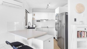 Une cuisine moderne avec des meubles blancs, un réfrigérateur en acier inoxydable et un petit îlot central doté d’un évier.