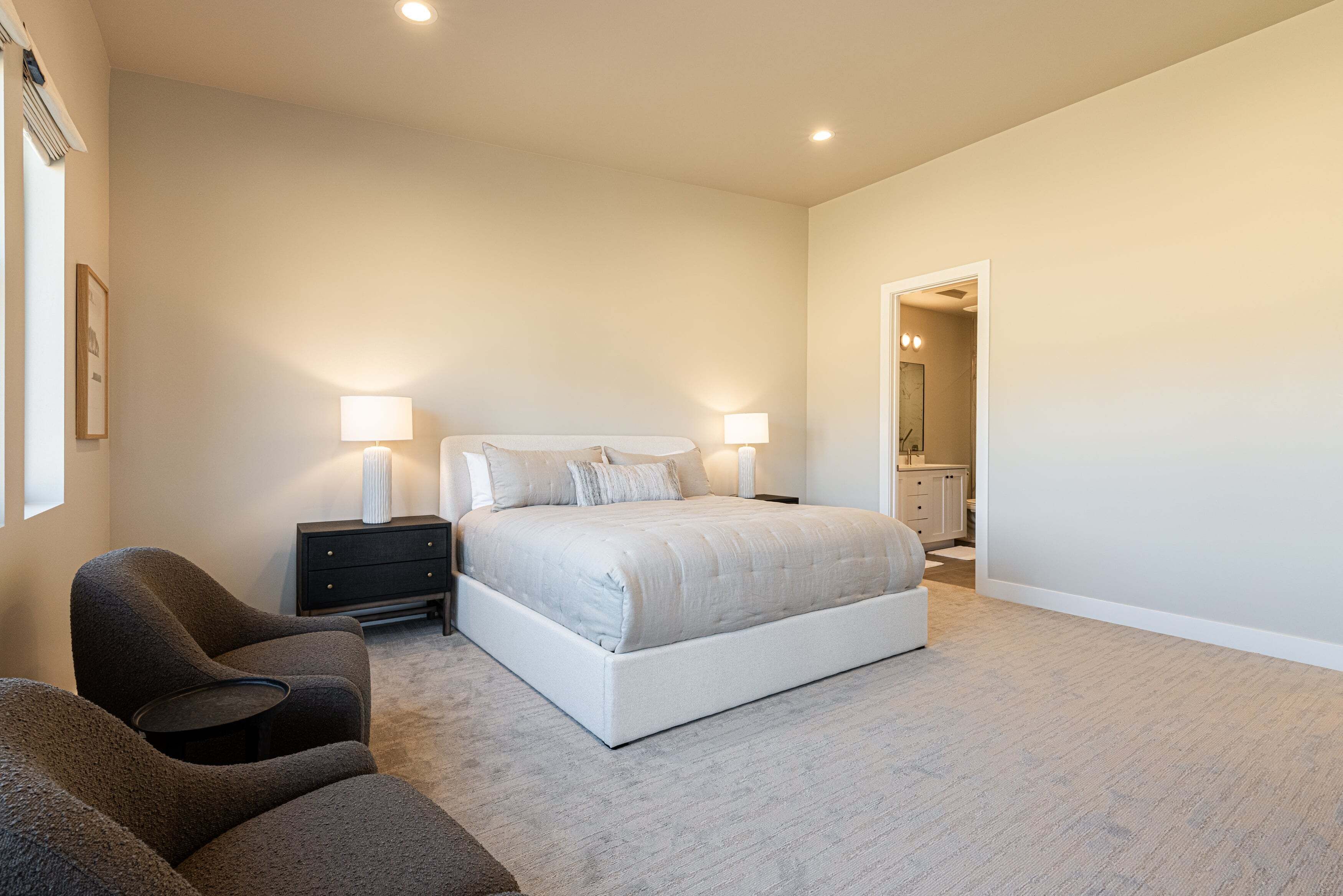A bedroom with a large bed, two bedside tables with lamps, a chair, and a dresser.