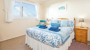 A bedroom with a bed, a nightstand, a window with curtains, a lamp, and a painting on the wall. - Ty Peggie, Holiday cottage Solva, Sleeps 4, 2 bedrooms,  bathrooms (Haverfordwest)
