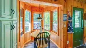 Interior de una cabaña de madera con una mesa de comedor y sillas, ventanas amplias y una puerta verde.