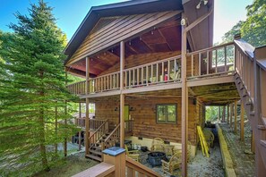 Eine zweistöckige Holzhütte mit Balkon, Sitzgelegenheit im Freien und einer Treppe.