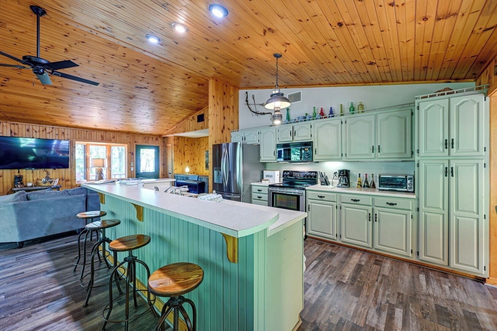 A spacious kitchen with wooden ceiling and walls, a central island with stools, and light green cabinets.