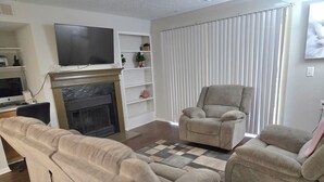 A living room with a fireplace, a television, and two armchairs. - 2-bed apartment, heart of RIO, Gaithersburg! Near 1-270, commuter convenient. (Gaithersburg)