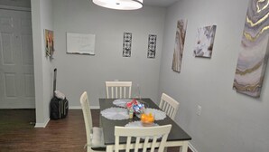 A dining area with a table set for four, surrounded by white chairs. There are decorative wall art pieces and a whiteboard on the wall. - 2-bed apartment, heart of RIO, Gaithersburg! Near 1-270, commuter convenient. (Gaithersburg)