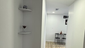 A narrow hallway with white walls and wooden flooring. There are two white shelves, one with a glass of red wine and the other with a glass of white wine. A table with chairs is visible in the distance. - Perfect terrace to relax, have a coffee or enjoy the Florida weather. (Tampa)