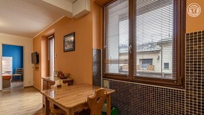 Ein Essbereich mit Holztisch und -stühlen, einem an der Wand montierten Fernseher und einem Fenster mit Jalousien.