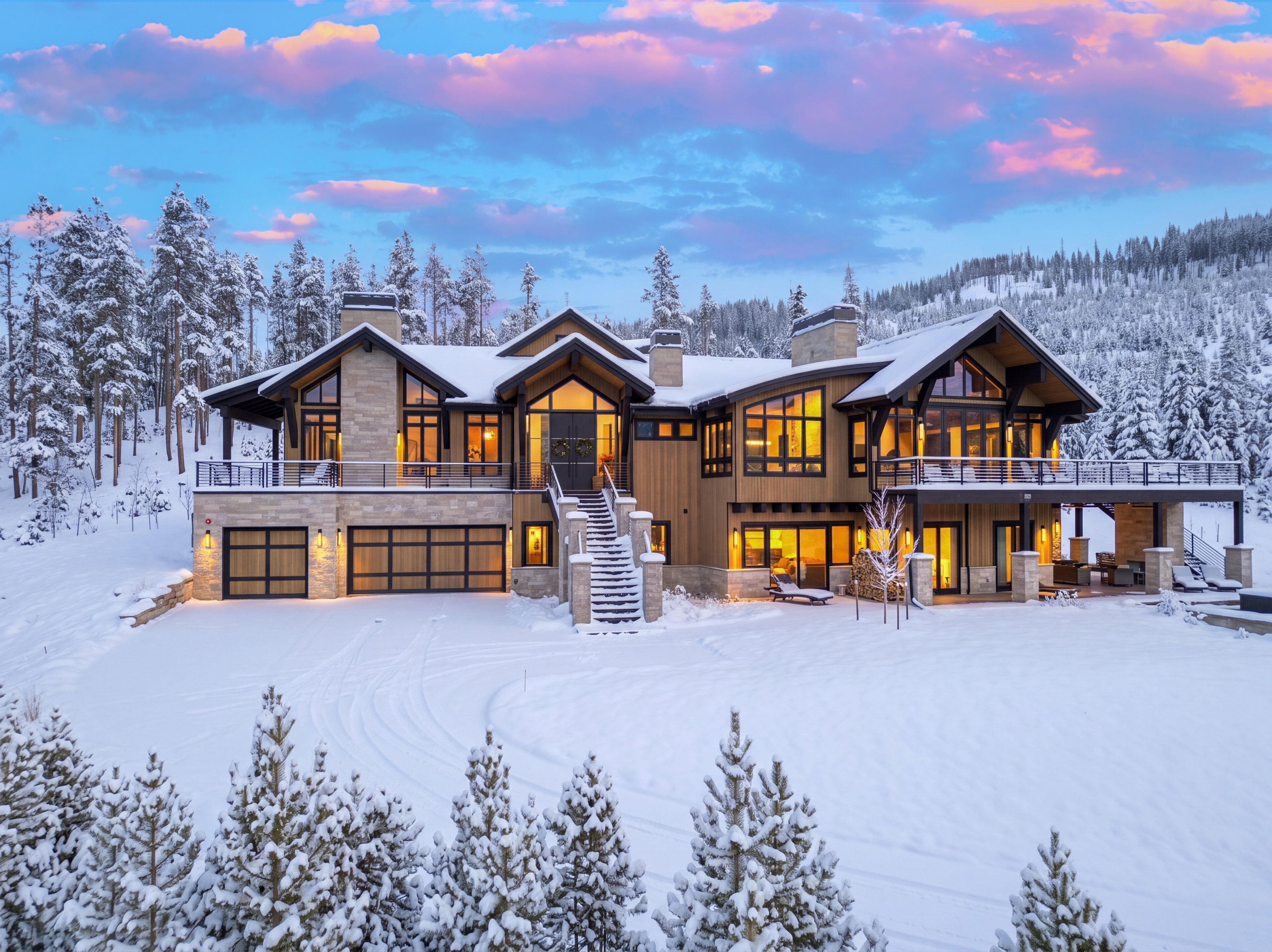A large, modern multi-story house with a garage, surrounded by snow-covered trees.
