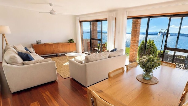 Ein modernes Wohnzimmer mit einem Holzespeisetisch, zwei Sofas und Meerblick durch große Fenster.