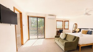 Ein Schlafzimmer mit einem Bett, einem grünen Sofa, einem Fernseher und einer Glastür, die auf einen Balkon führt.