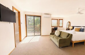 A bedroom with a bed, a green sofa, a TV, and a sliding glass door leading to a balcony. - Banyandah - home on the water (Marks Point)