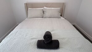 Een net opgemaakt bed met een opgerolde handdoek in het midden, een hoofdbord en beddengoed met een patroon.