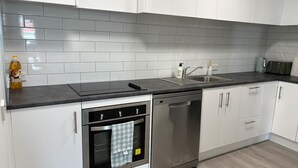 Een moderne keuken met witte kastjes, een zwart aanrecht, een RVS vaatwasser en een betegelde spatwand.