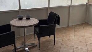 En täckt uteplats med ett runt bord, två stolar och en takfläkt.