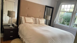 Un letto rifatto con una testiera, un comodino con una lampada, e vista sul verde circostante.