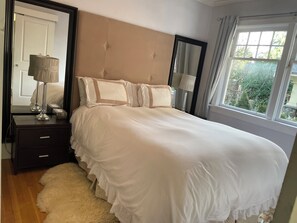 Ein ordentlich gemachtes Bett mit Kopfteil, ein Nachttisch mit Lampe und Blick ins Grüne.