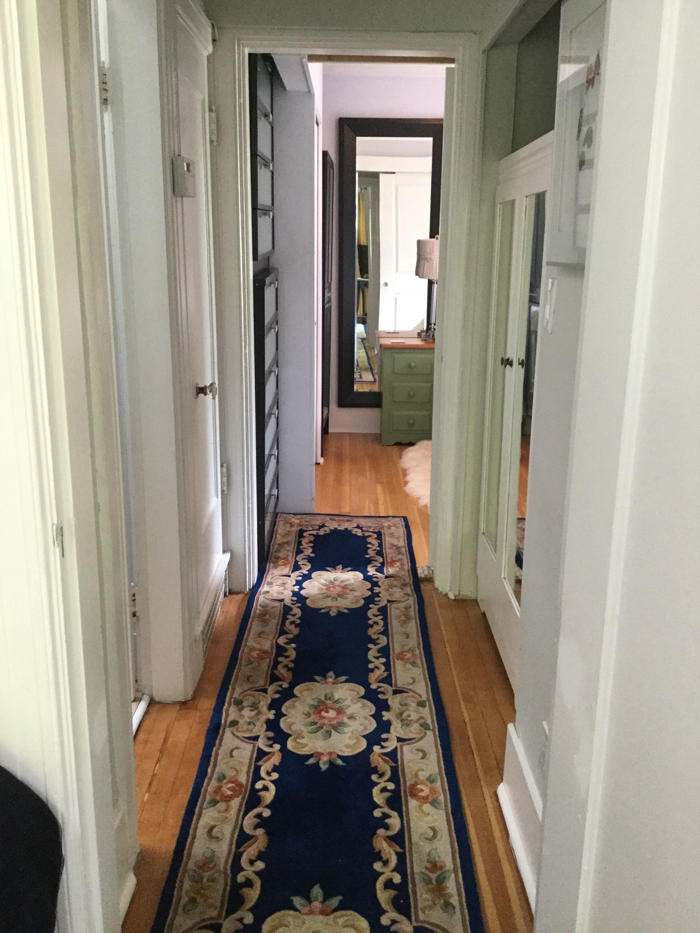 A hallway with a blue floral carpet, wooden flooring, and white walls.