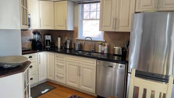 A kitchen with light-colored cabinets, a stainless steel refrigerator, a dishwasher, and a coffee maker.