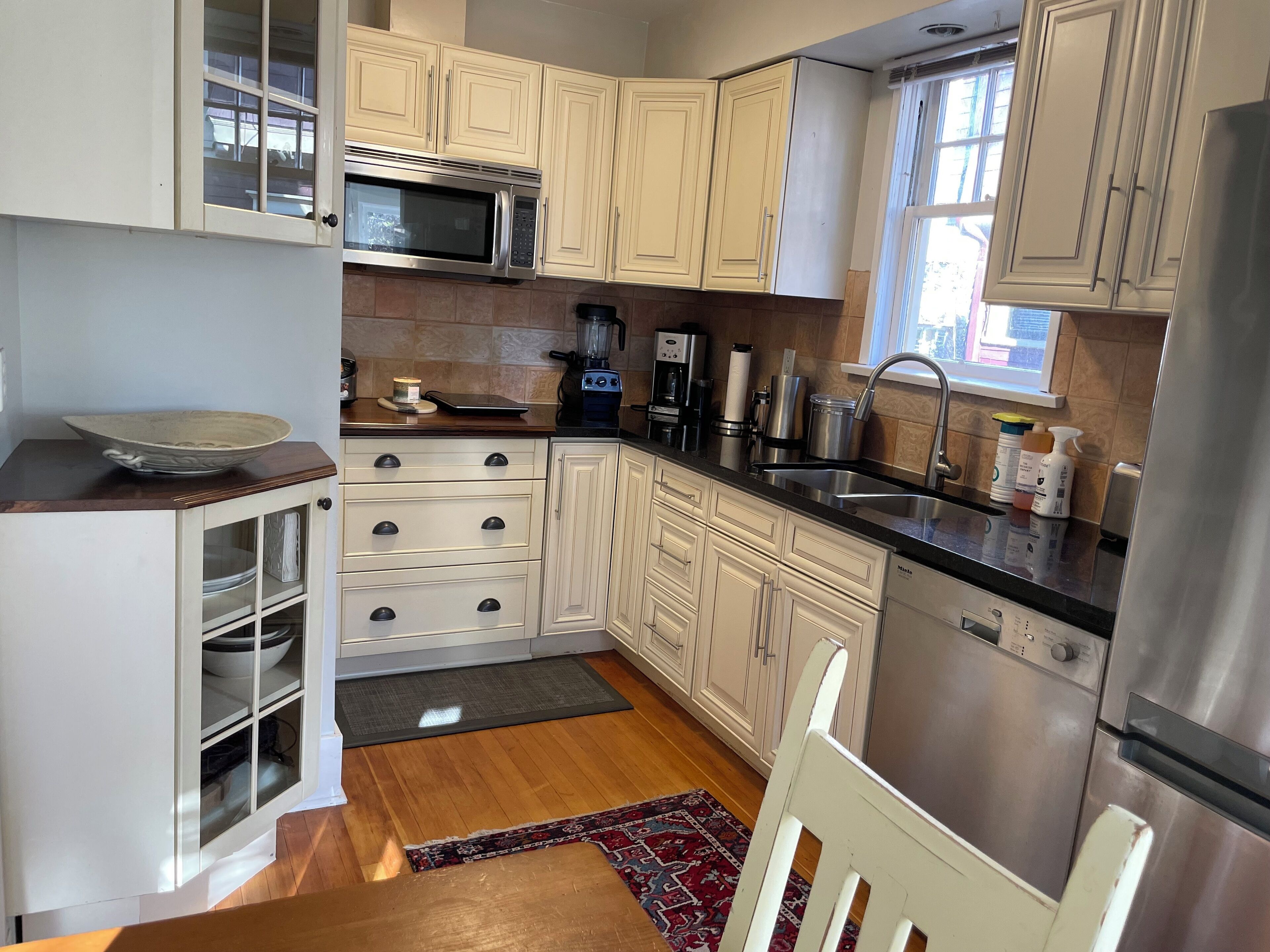 A modern kitchen with white cabinetry, stainless steel appliances, and a wooden floor.