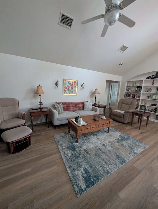 Un salon comprenant un canapé, des fauteuils, une table basse, un ventilateur de plafond et une bibliothèque.