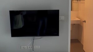Quarto com TV montada, uma unidade de entretenimento branca embaixo e um aparelho de ar condicionado em cima.