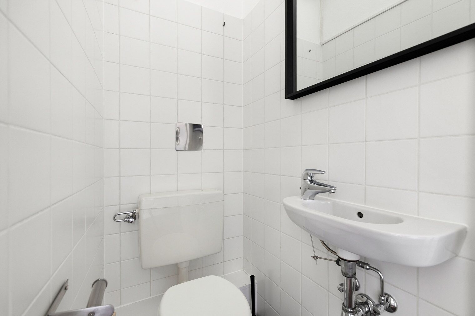 A modern bathroom with white tiles, a toilet, a sink, and a mirror.