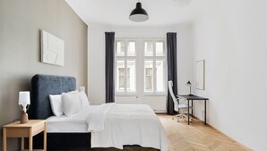 A modern bedroom with a bed, bedside table, desk, chair, and a large window with curtains. - Blueground | Wieden, view, nr Belvedere (Vienna)