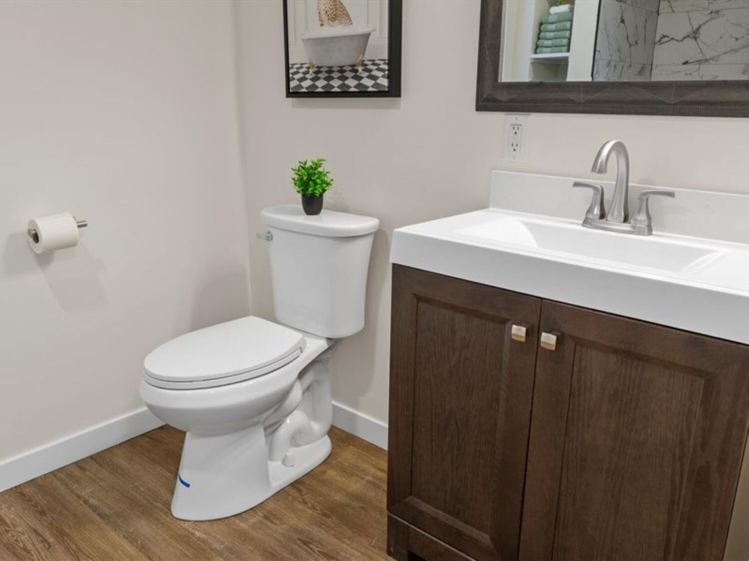 Ein modernes Badezimmer mit Toilette, Holzschrank, Waschbecken und einer kleinen Topfpflanze.