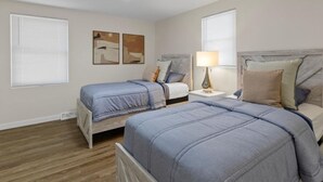 A bedroom with two beds, a nightstand with a lamp, and artwork on the wall.