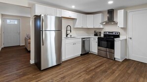 A modern kitchen with white cabinets, stainless steel appliances, and a wooden floor.