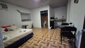 Une pièce de taille modeste comprenant un lit, une petite table, une chaise, un coin cuisine et une salle de bain.