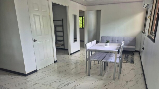 Une pièce dotée d’un sol en marbre, d’une table blanche avec quatre chaises, d’un canapé gris et d’une porte donnant sur une autre pièce.
