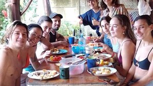 Un groupe de personnes est assis autour d’une table en bois à l’extérieur, et elles mangent et boivent.