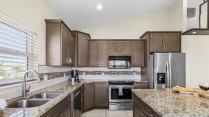 Cocina moderna con encimeras de granito, electrodomésticos de acero inoxidable y armarios de madera oscura.