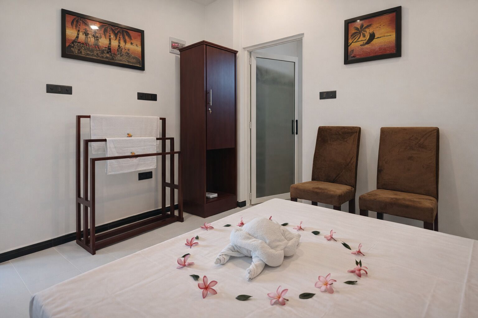 Habitación de hotel con cama, dos sillas, armario y obras de arte en las paredes.